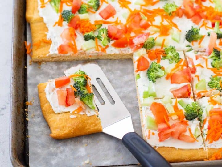 A veggie pizza has been sliced and served with a small spatula.