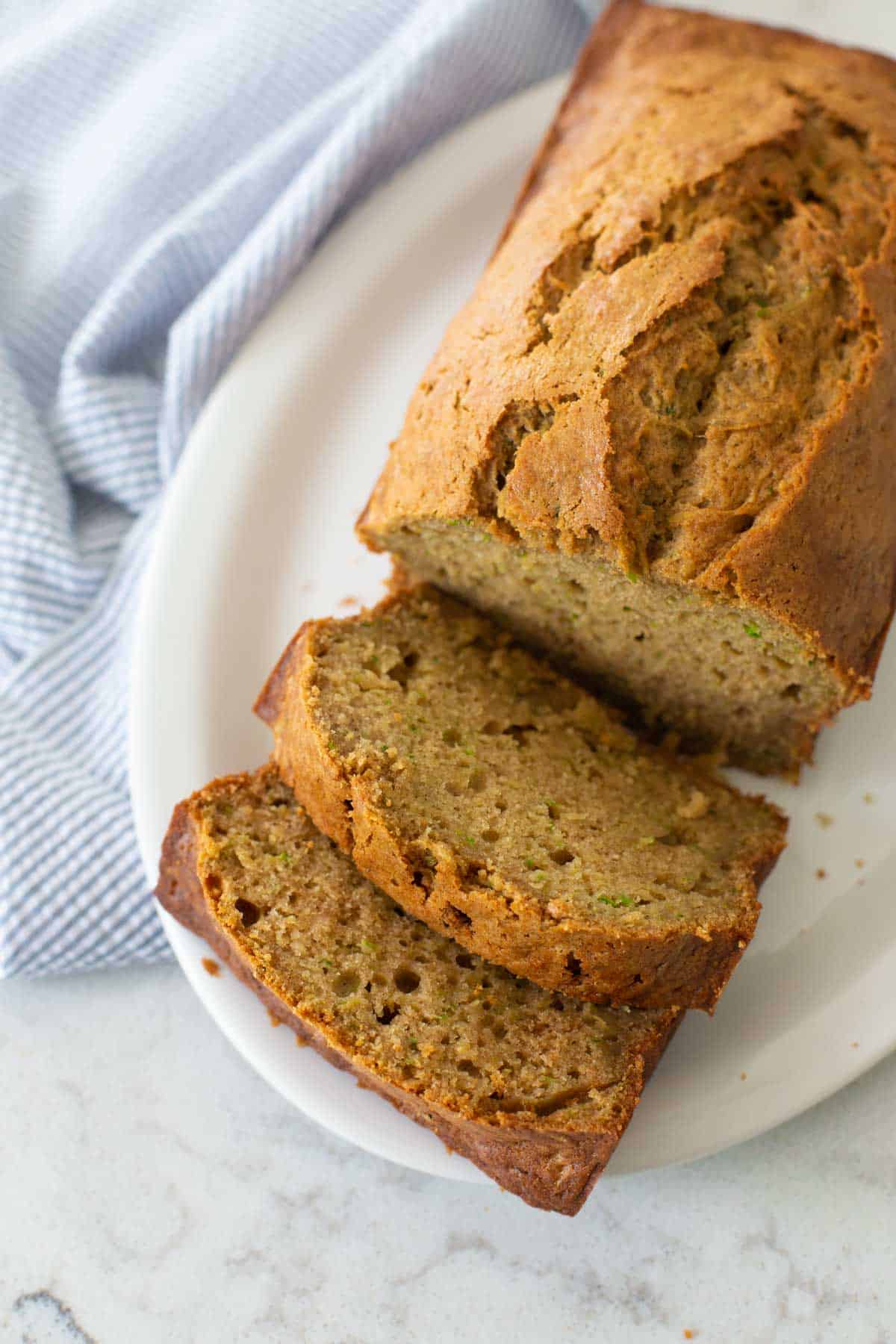 A sliced loaf of zucchini bread is served on a white plate next to a blue napkin.