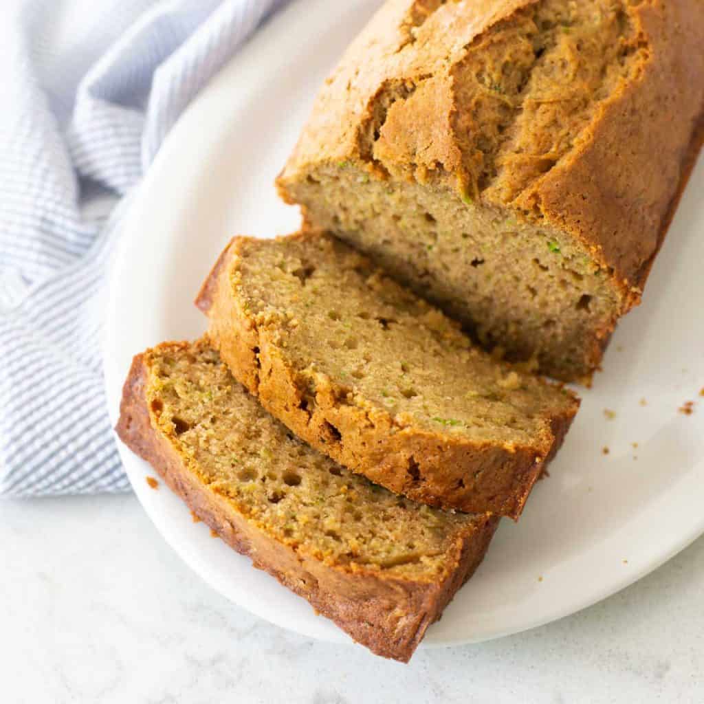 A platter of sliced zucchini bread sits next to a blue napkin.