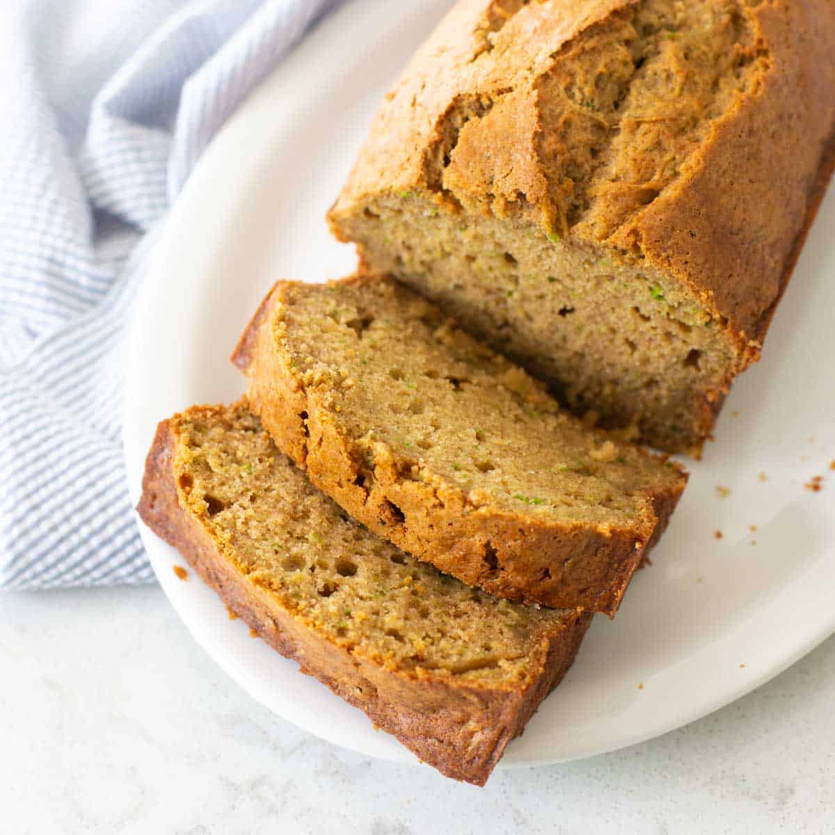 A platter of sliced zucchini bread sits next to a blue napkin.