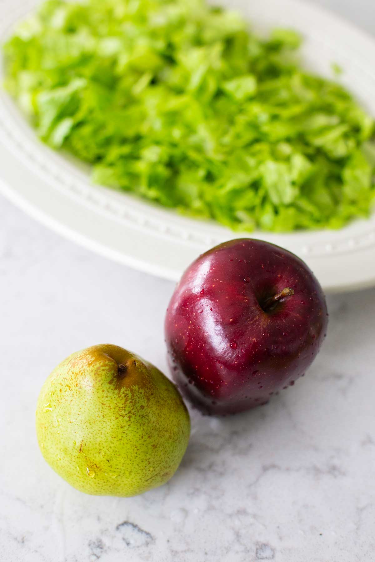 An apple and a pear sit in front of a platter of lettuce.