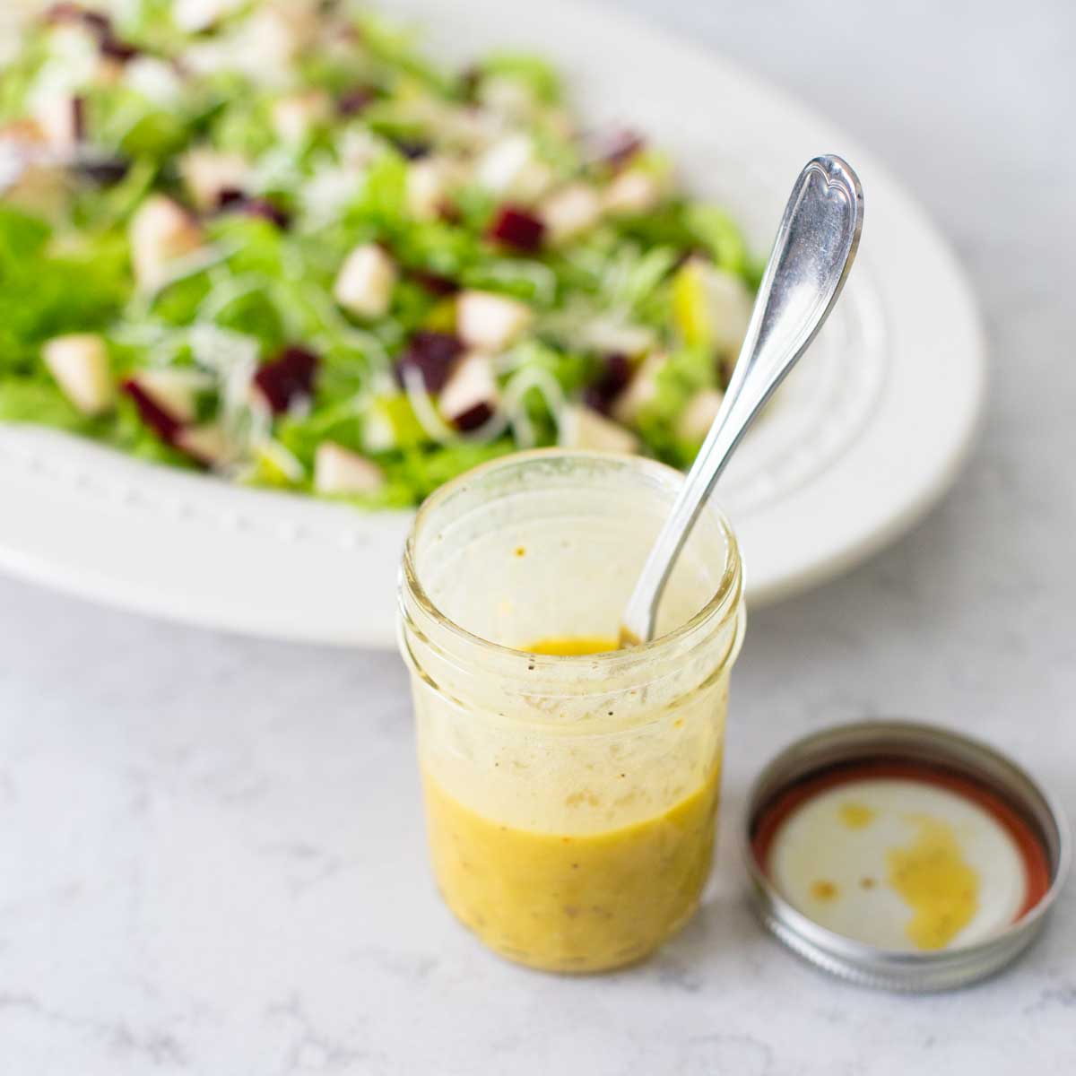 A mason jar filled with mustard vinaigrette is in front of a salad.