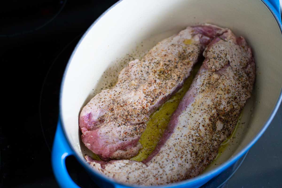 The raw pork tenderloins are being browned in a dutch oven.
