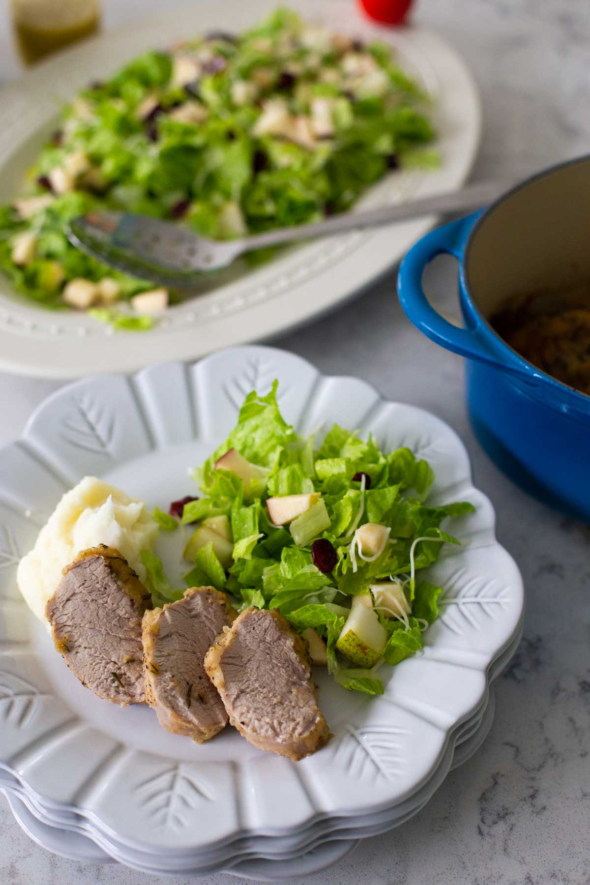The pork has been sliced and served on a plate with a green salad and mashed potatoes.