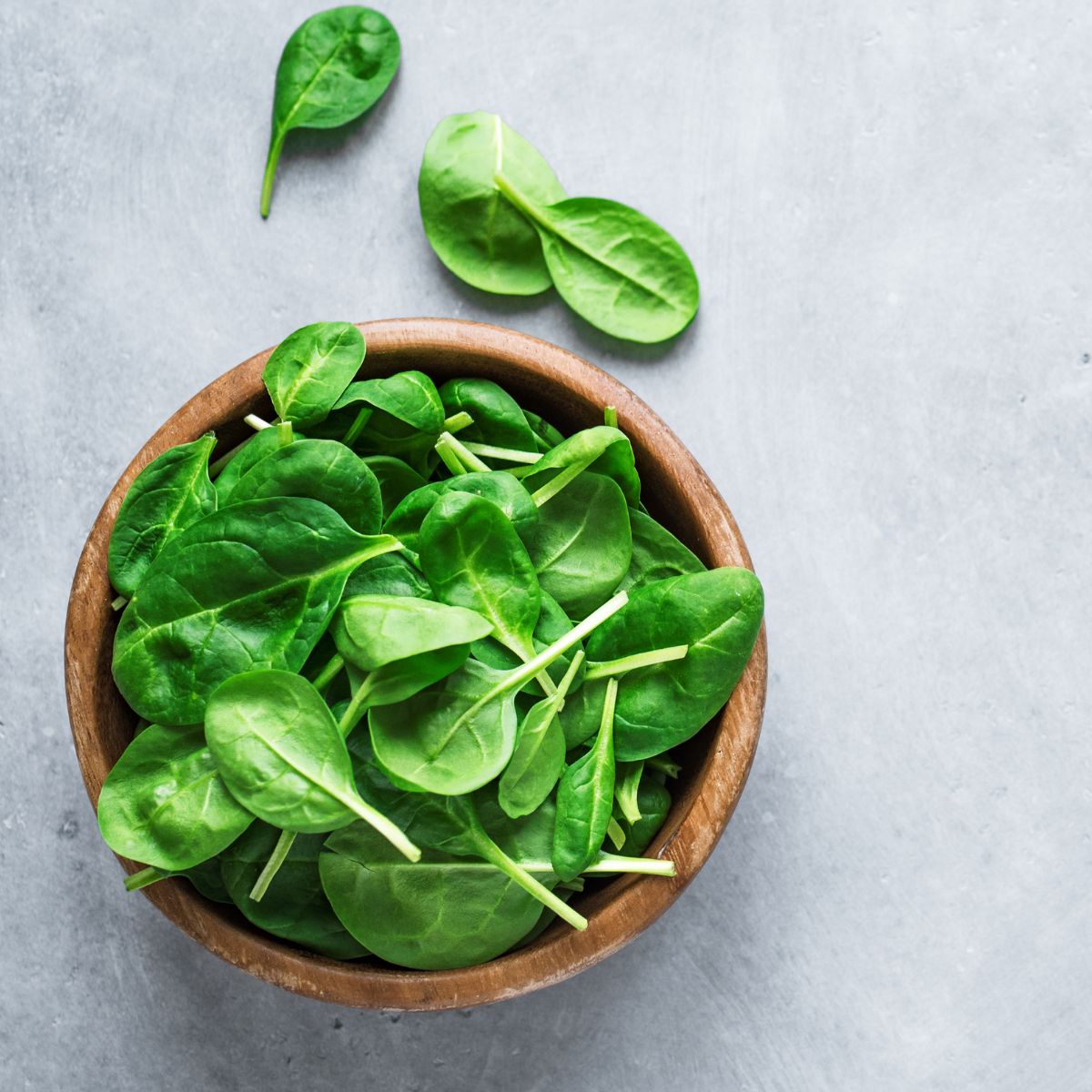A brown bowl filled with raw baby spinach leaves.