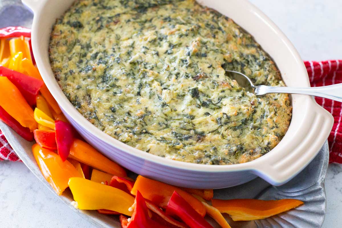 The hot spinach and artichoke dip is served on a platter with red bell peppers.