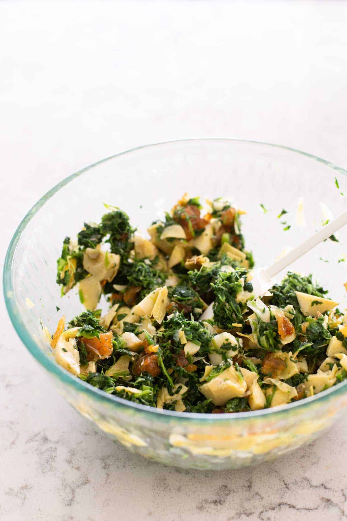 The spinach and artichokes have been stirred together in a large mixing bowl.