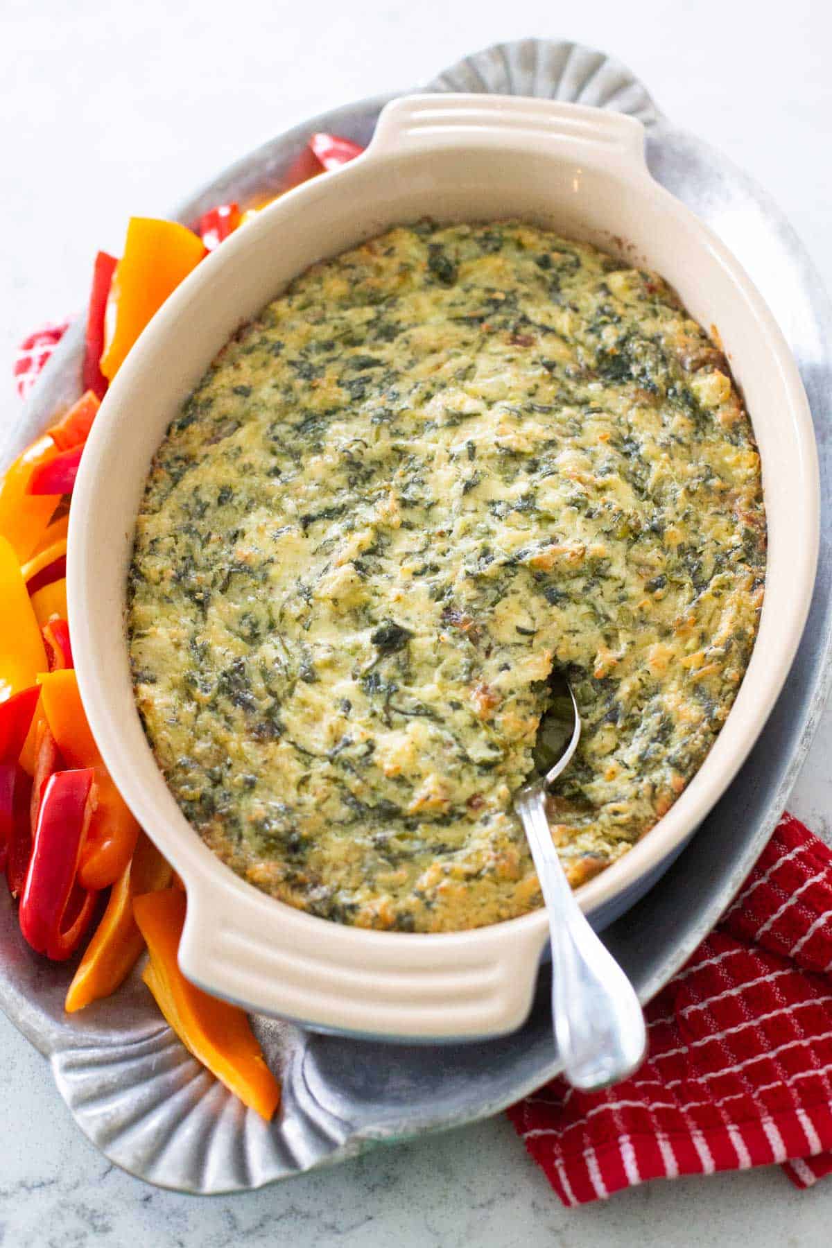 The finished baked artichoke dip is being served on a platter with raw bell peppers.