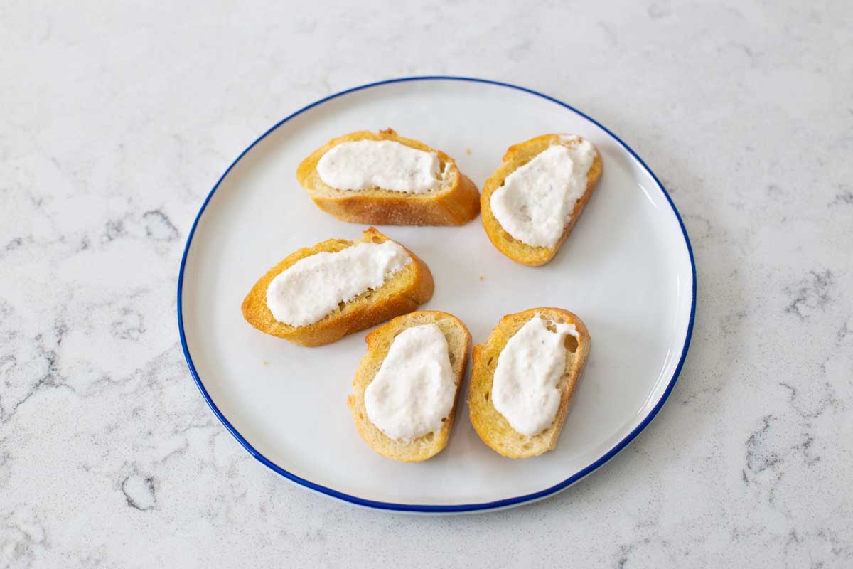 A plate of crostini have a layer of horseradish sauce spread on each piece of toast.