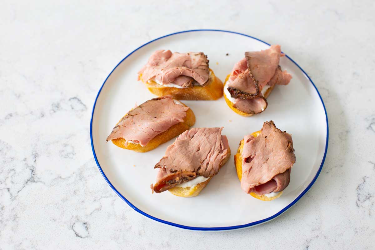 Slices of thick cut roast beef have been added to each crostini.