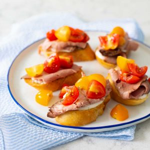 A plate of roast beef crostini with horseradish cream and cherry tomatoes.