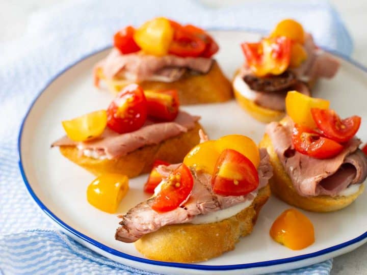 A plate of roast beef crostini with horseradish cream and cherry tomatoes.