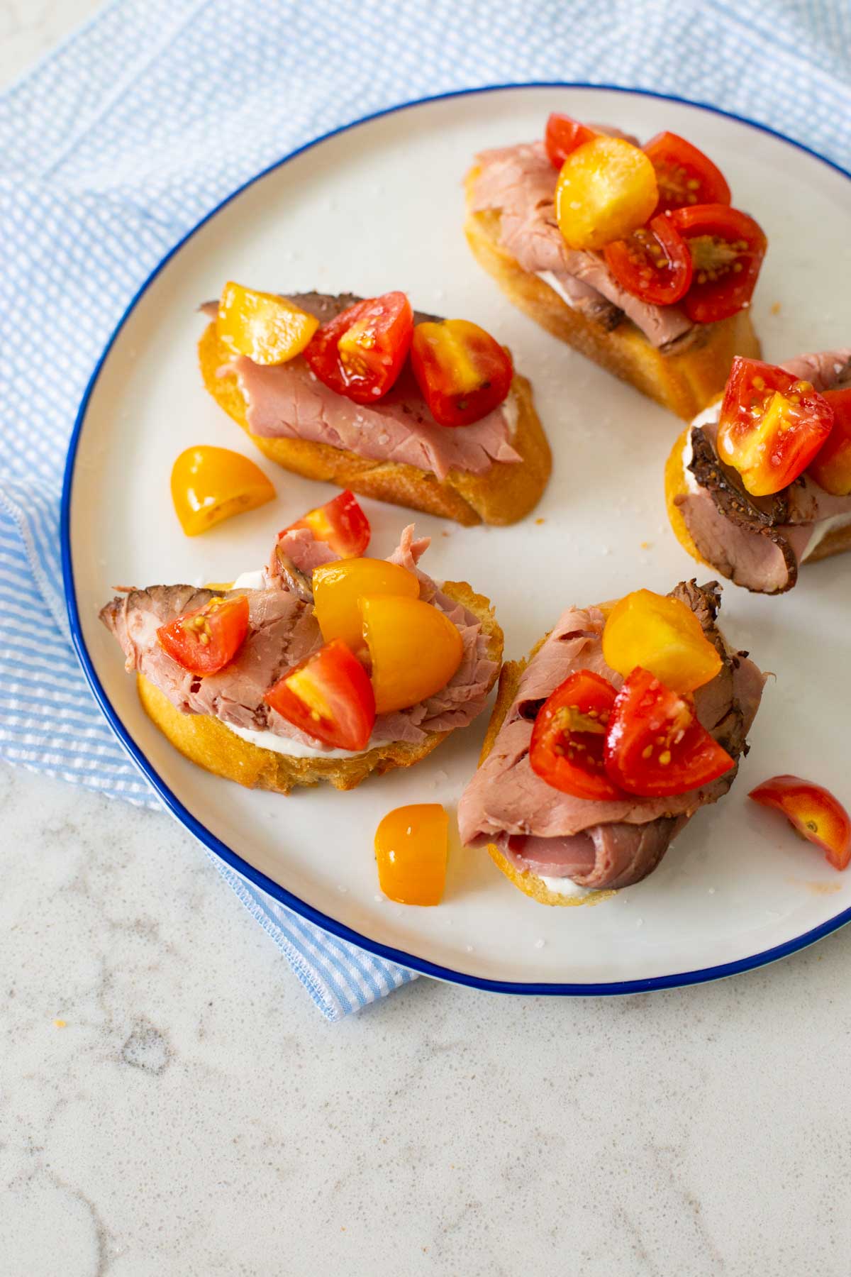 Yellow and red cherry tomatoes have been chopped and sprinkled over the beef crostini.