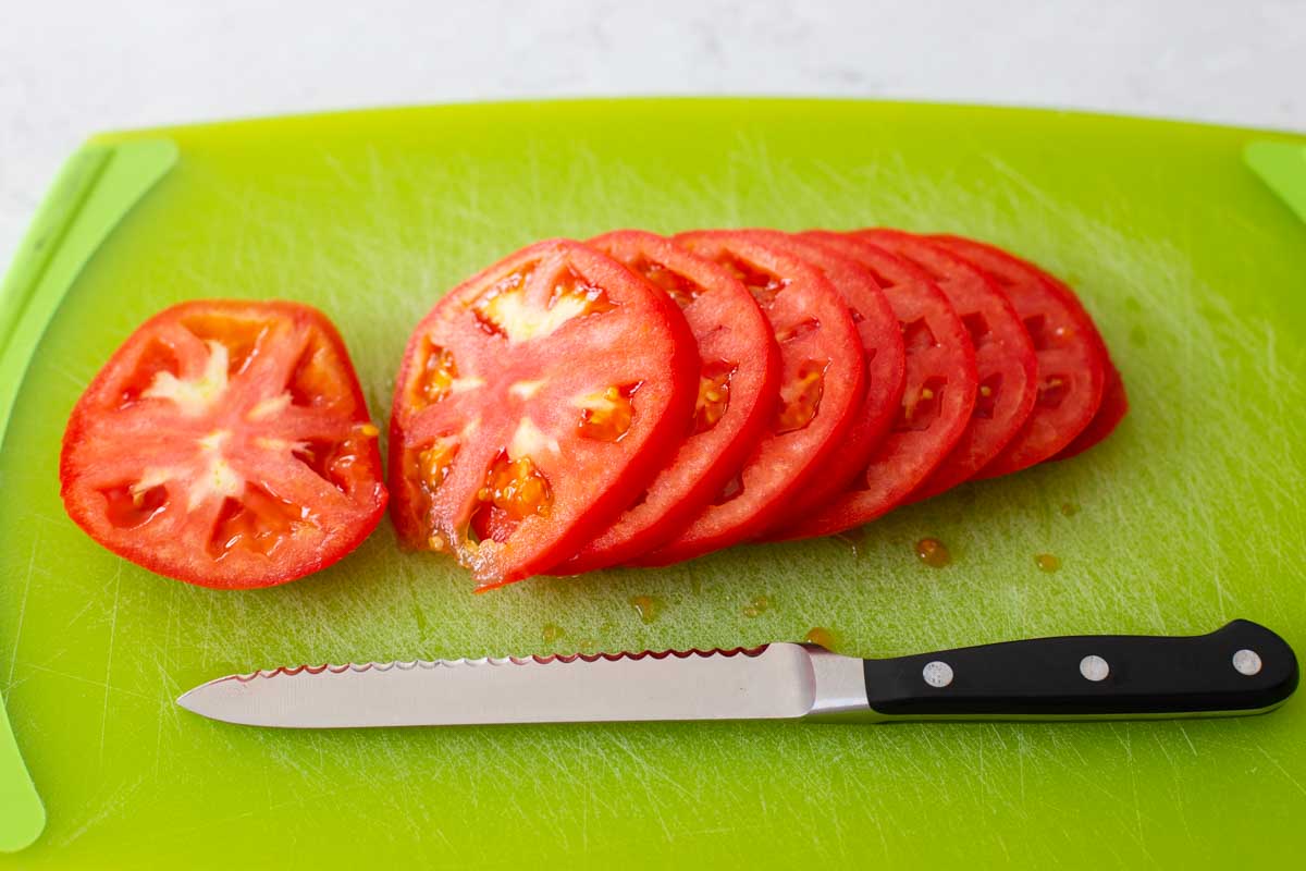 A red tomato has been sliced on a cutting board with a serrated knife.