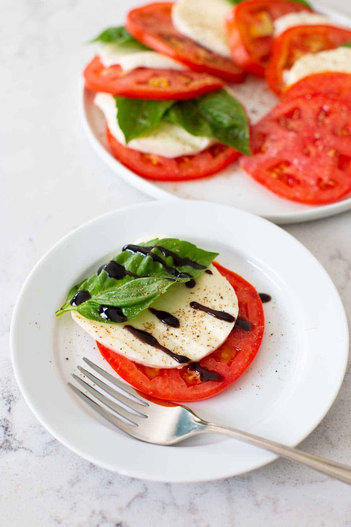 A serving of tomato caprese drizzled with balsamic vinegar is on a plate with a fork.