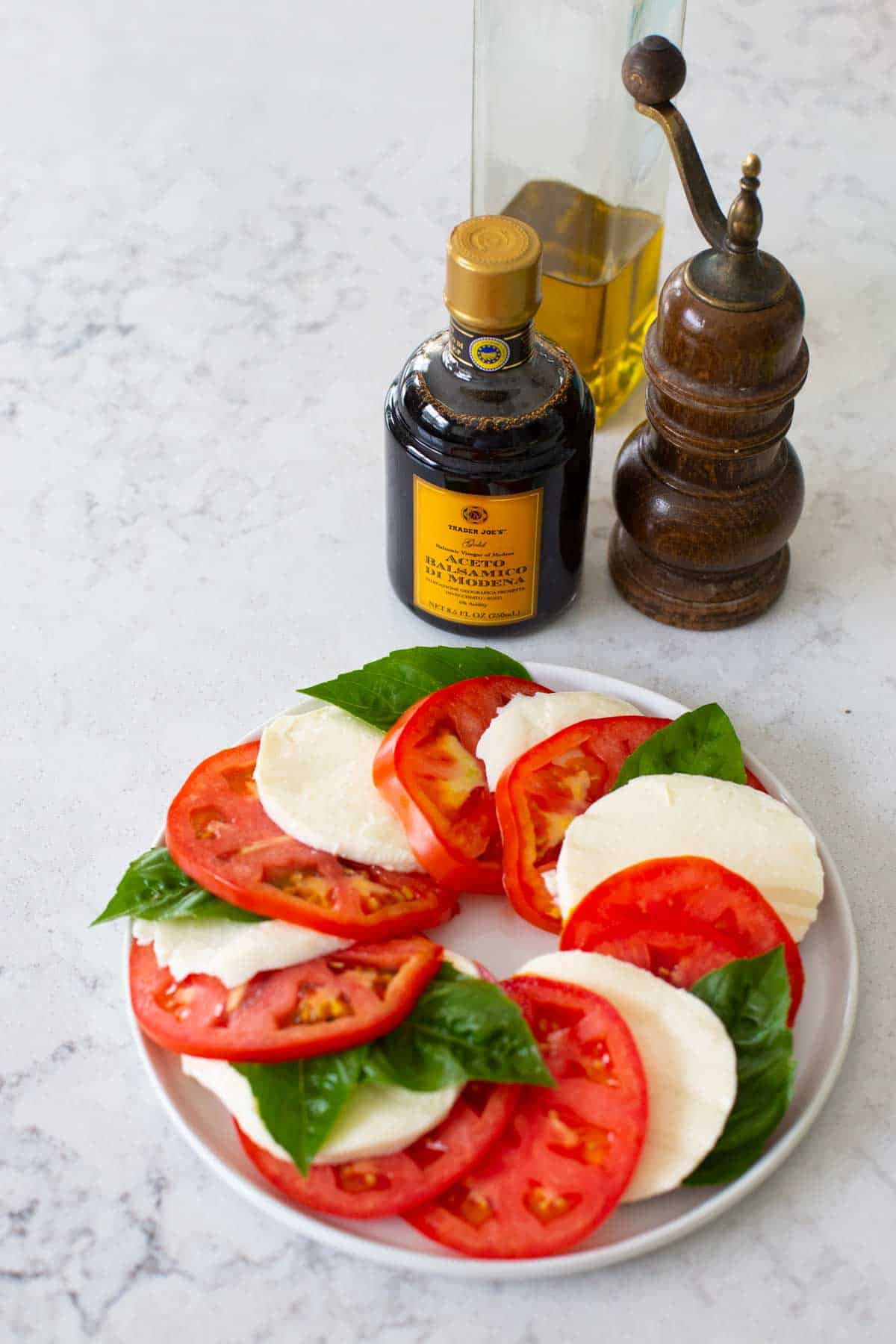 The fresh basil has been added to the platter. Bottles of balsamic vinegar and olive oil with a pepper grinder are in the background.