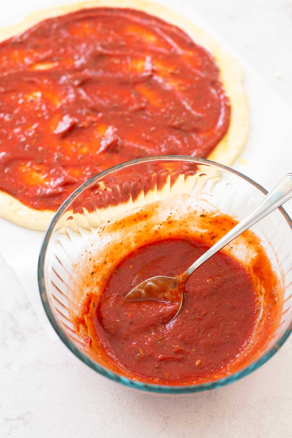 The pizza sauce is being spread onto a homemade pizza crust.