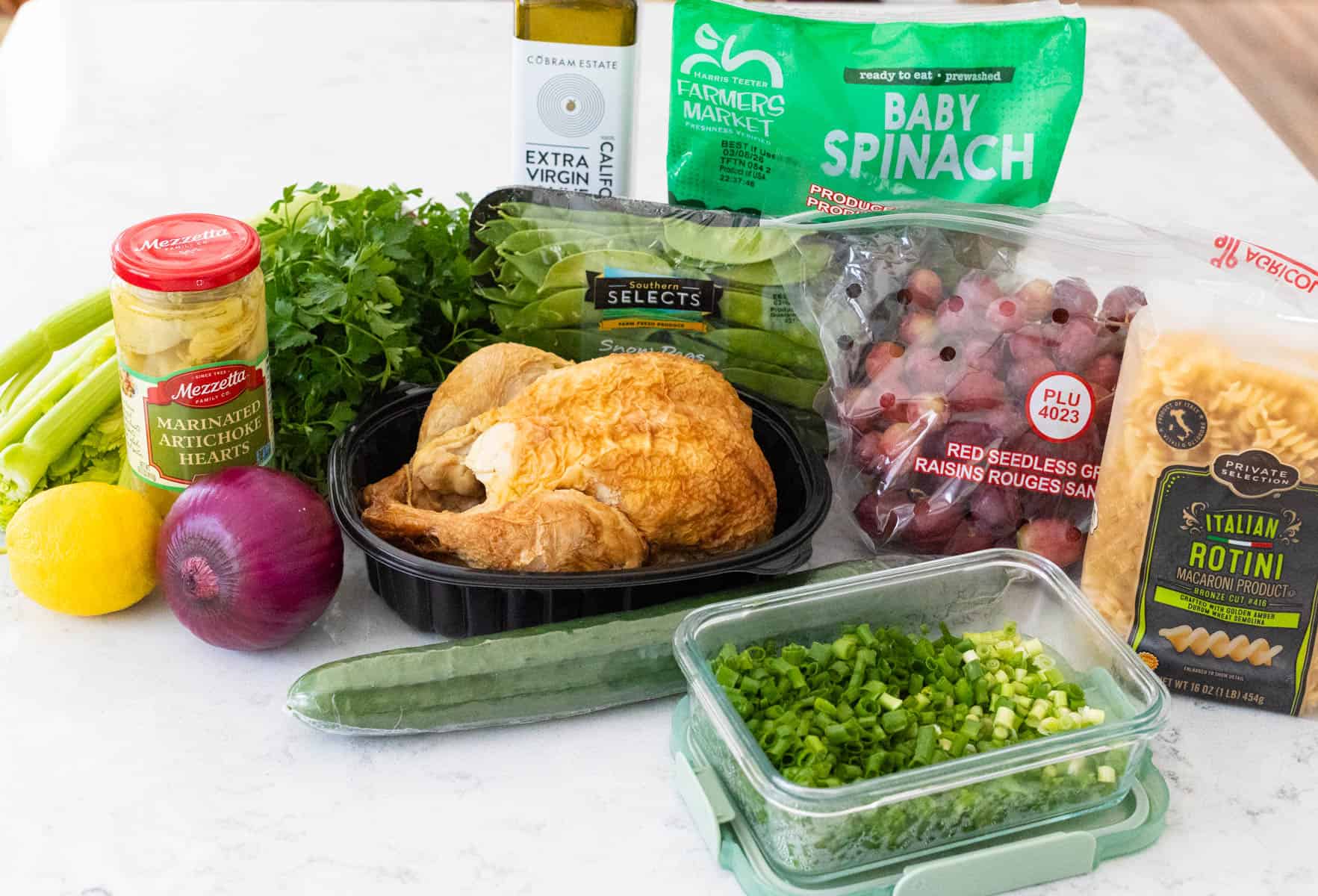 The rotisserie chicken is on the counter surrounded by the ingredients needed to make the salad.