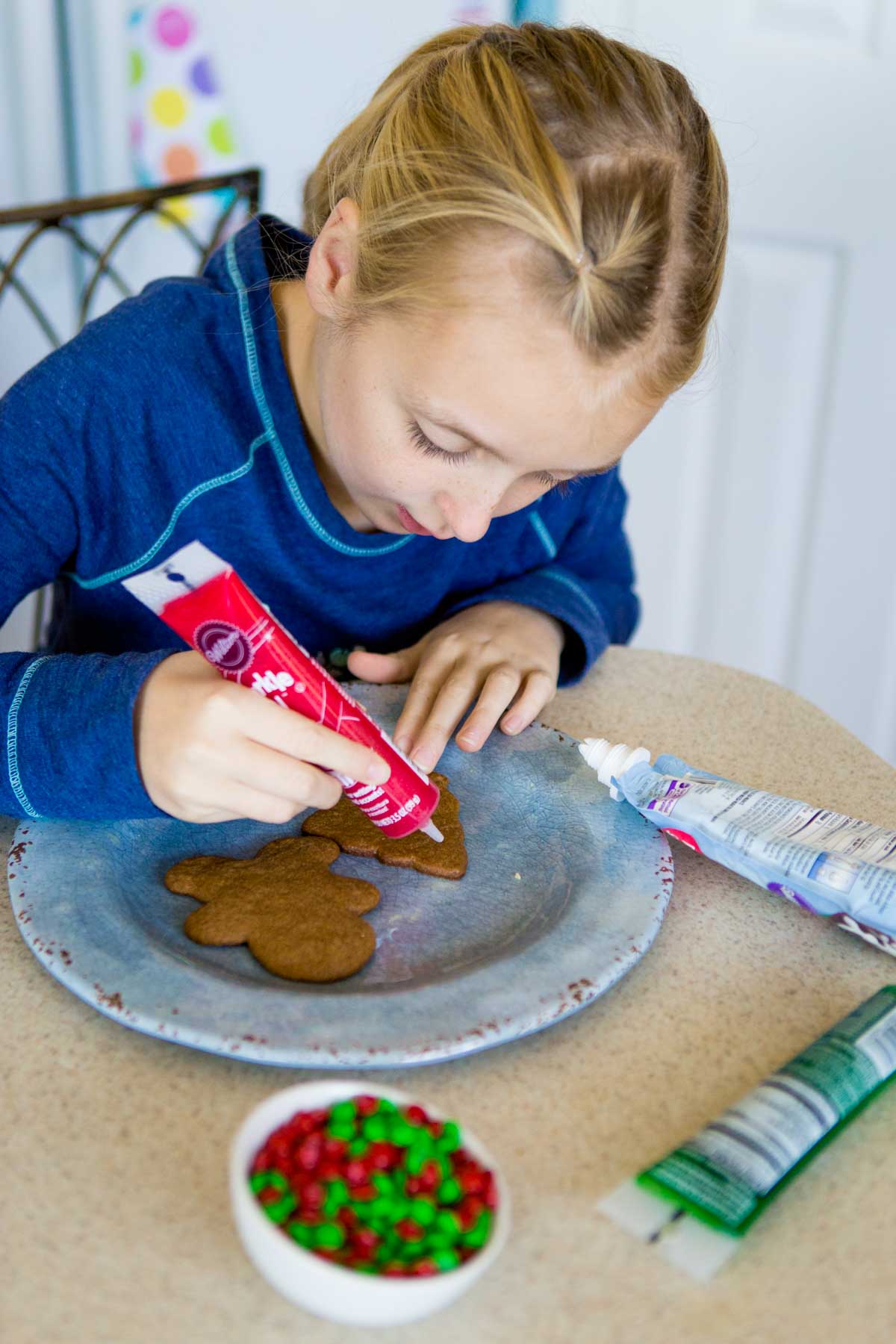 A young girl decorates a gingerbread cookie with icing.