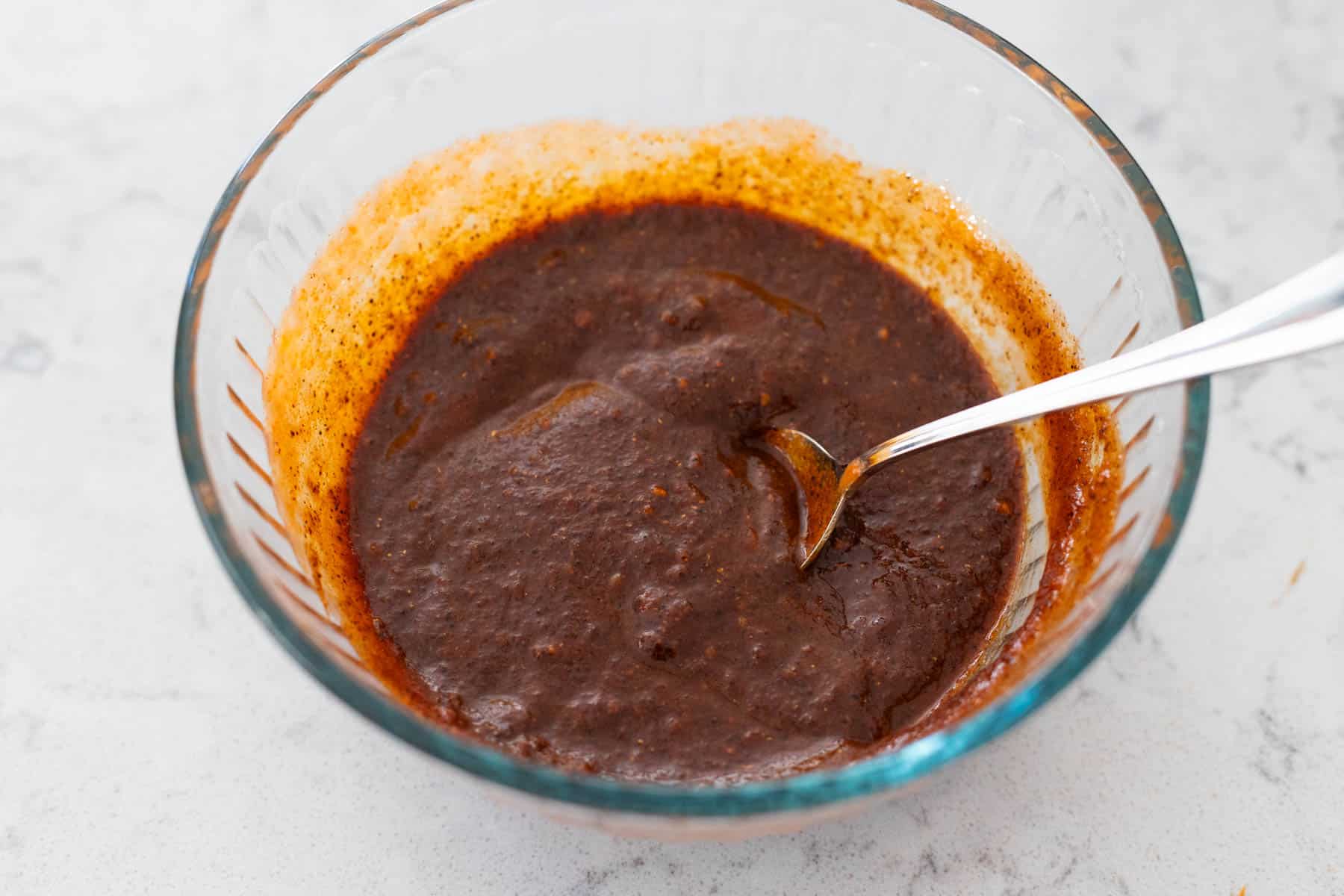 The tomato sauce has been stirred into the spices in a mixing bowl.