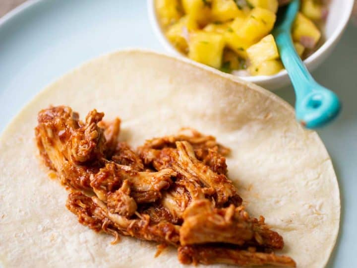 Shredded chicken meat on a taco shell has a tomato based sauce.