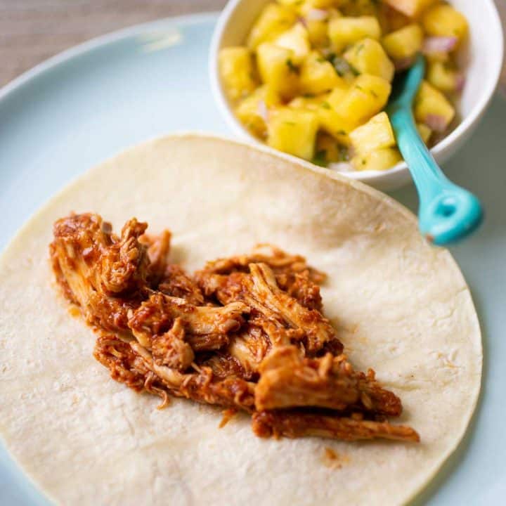Shredded chicken meat on a taco shell has a tomato based sauce.