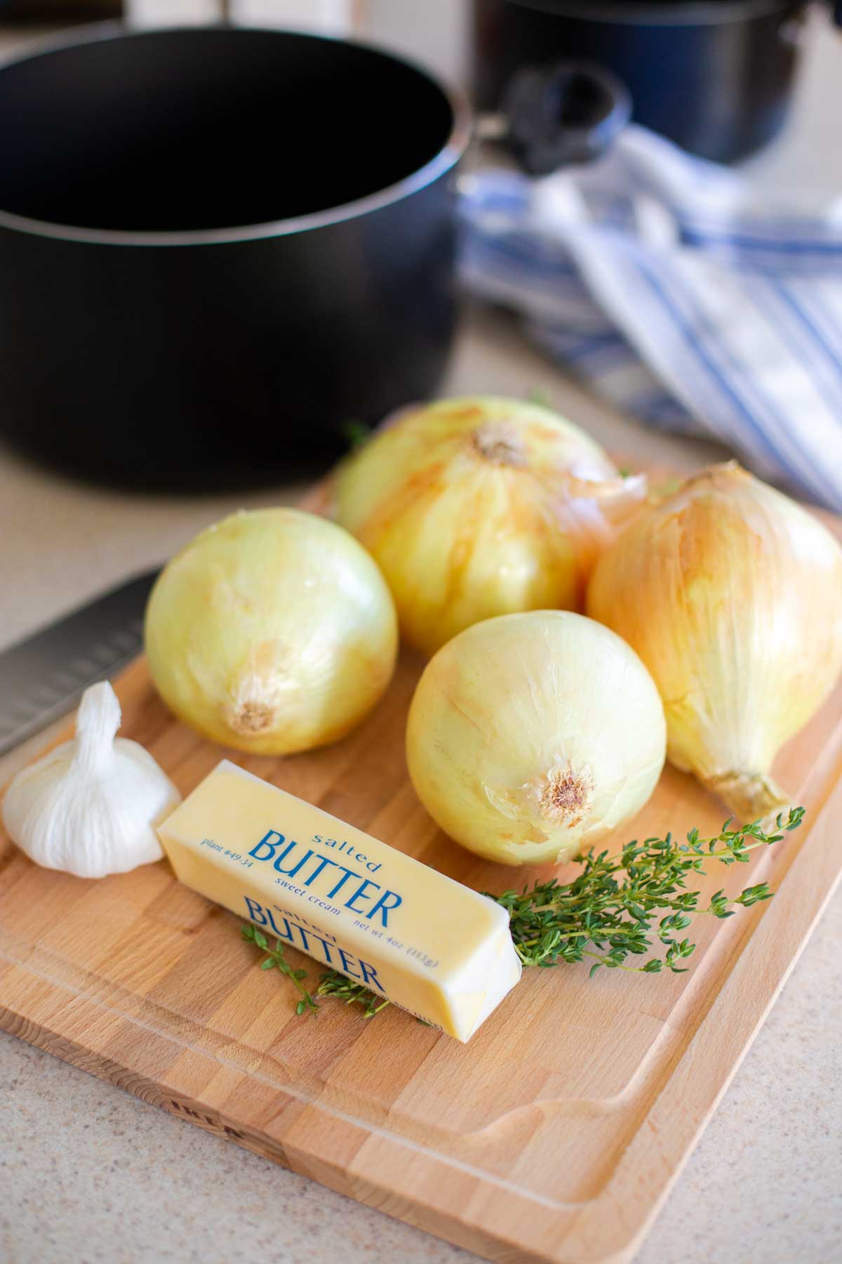The onions and butter and herbs and garlic are on a cutting board.