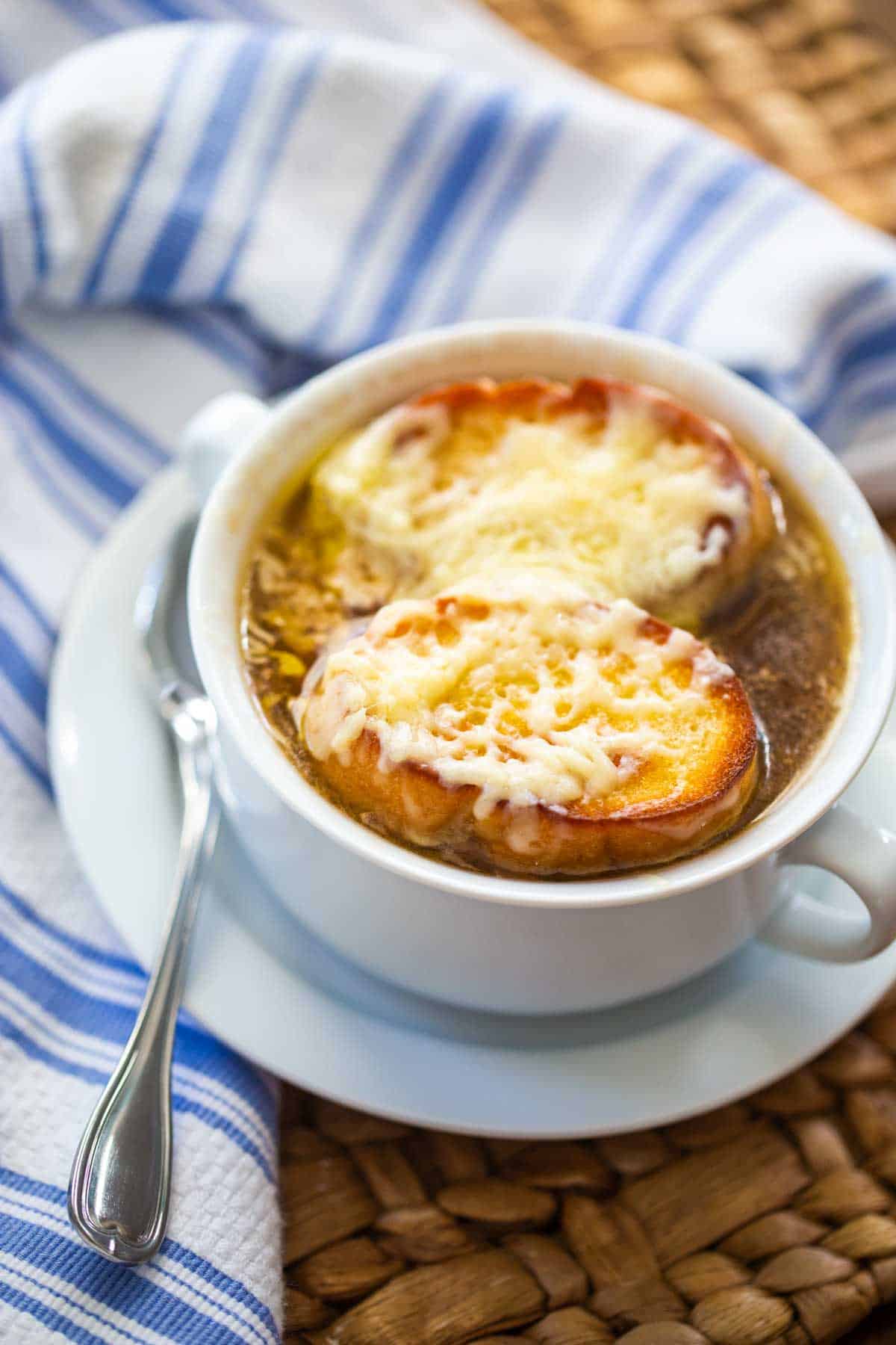 A bowl of French onion soup has melted cheese and a toasted baguette.