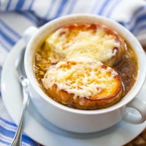 A bowl of French onion soup has toasted baguette slices with melted cheese over the top.