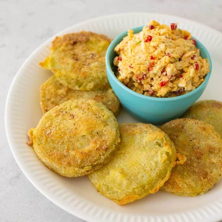 A serving of fried green tomatoes has a bowl of pimento cheese for topping.