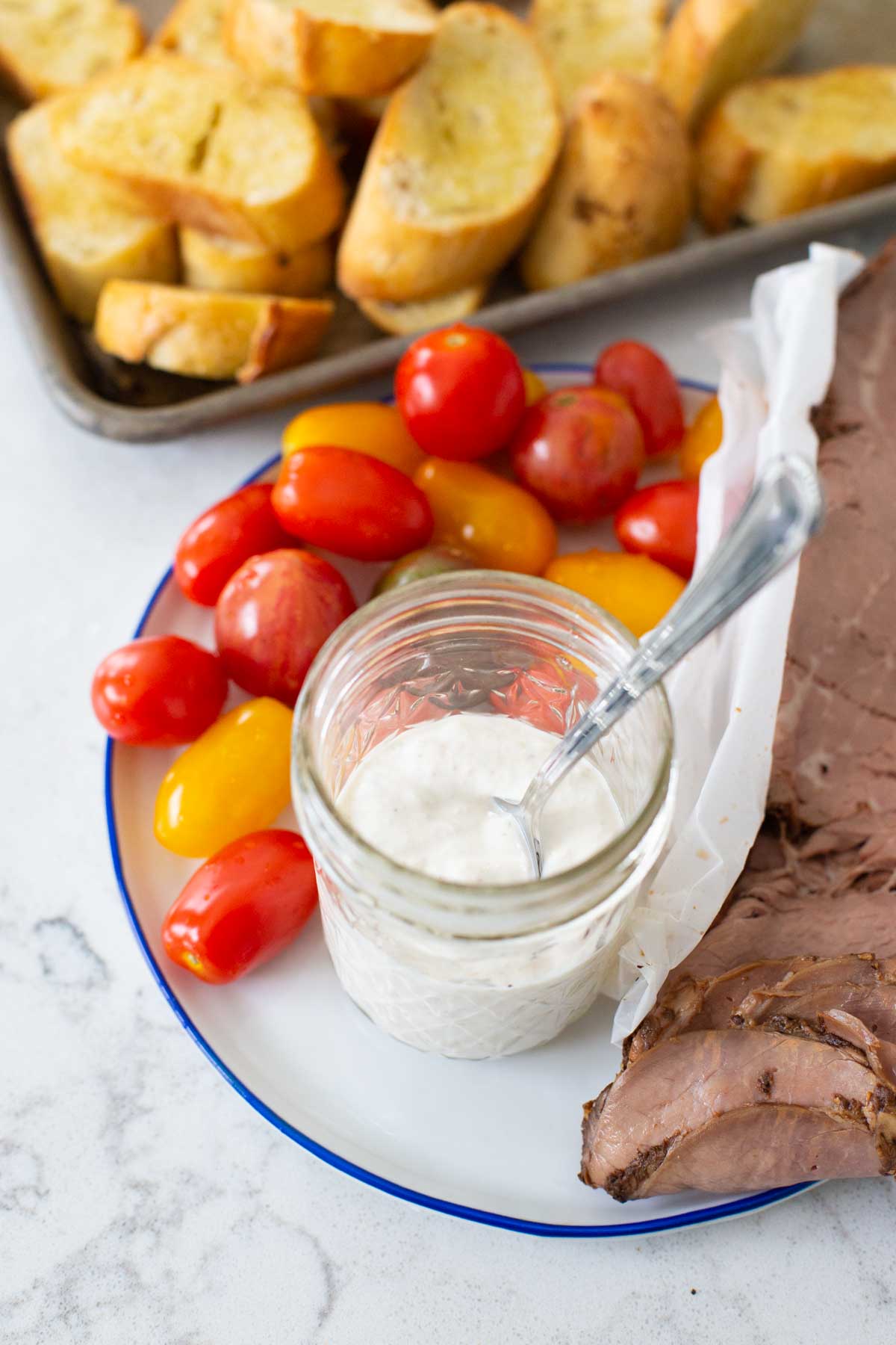 The horseradish sauce sits on a plate next to the roast beef, cherry tomatoes, and a platter of crostini.
