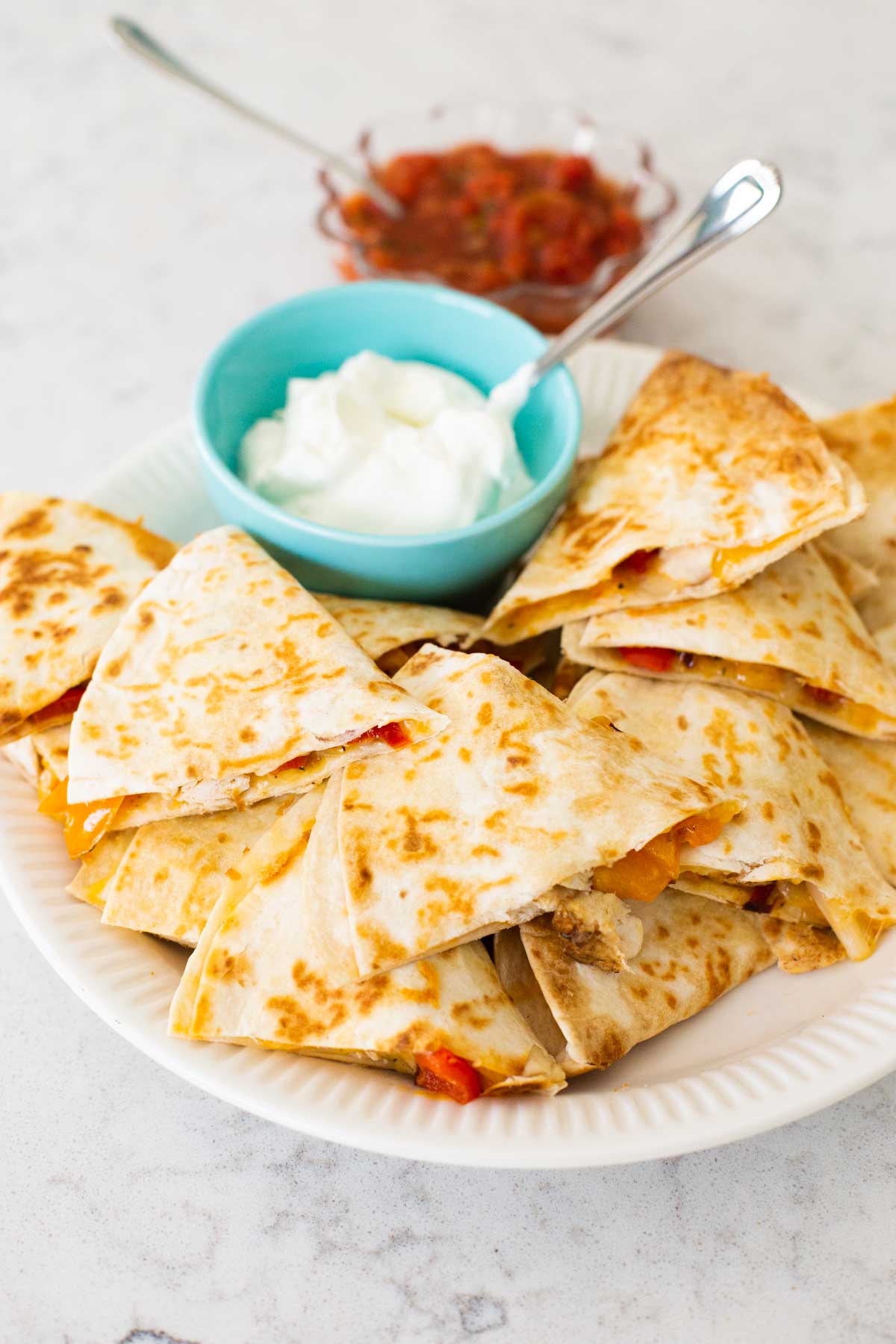 A platter of chicken quesadillas with a bowl of sour cream and salsa.