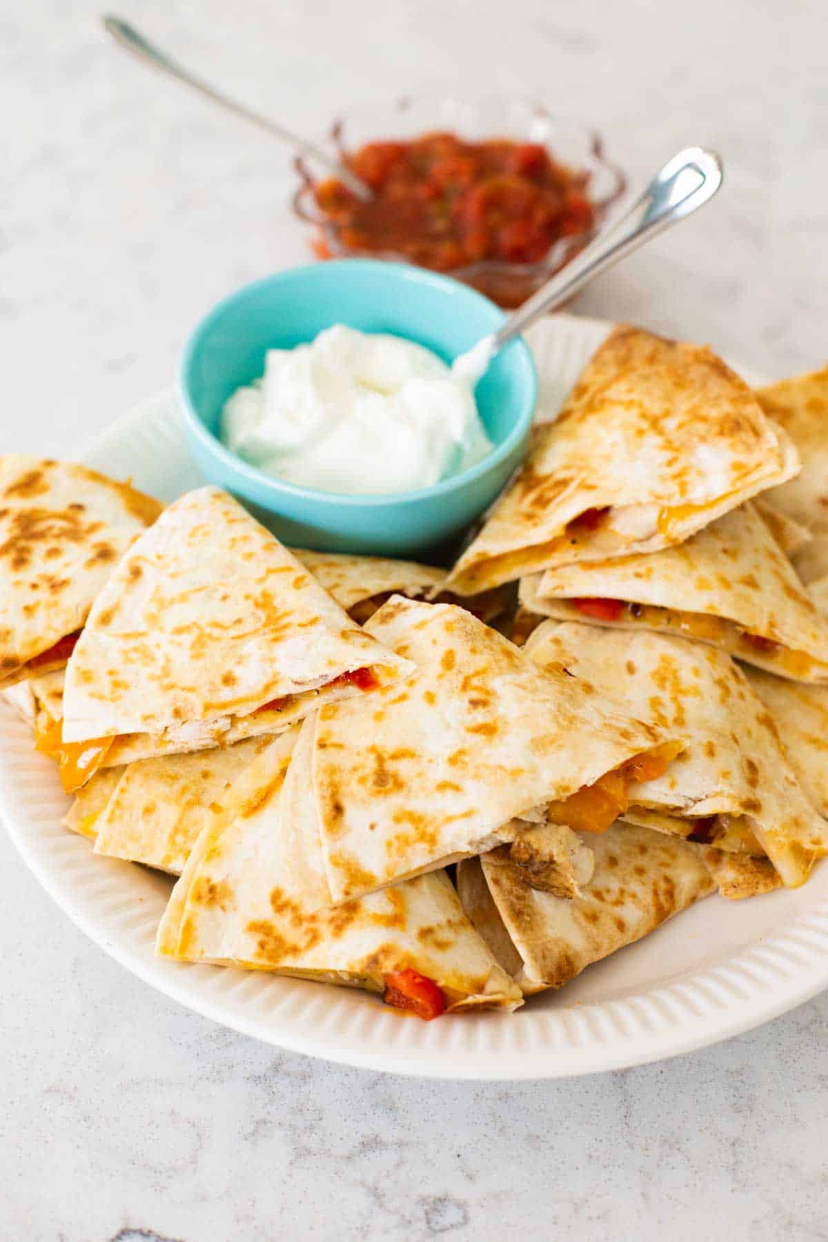 A platter of chicken quesadillas with a bowl of sour cream and salsa.