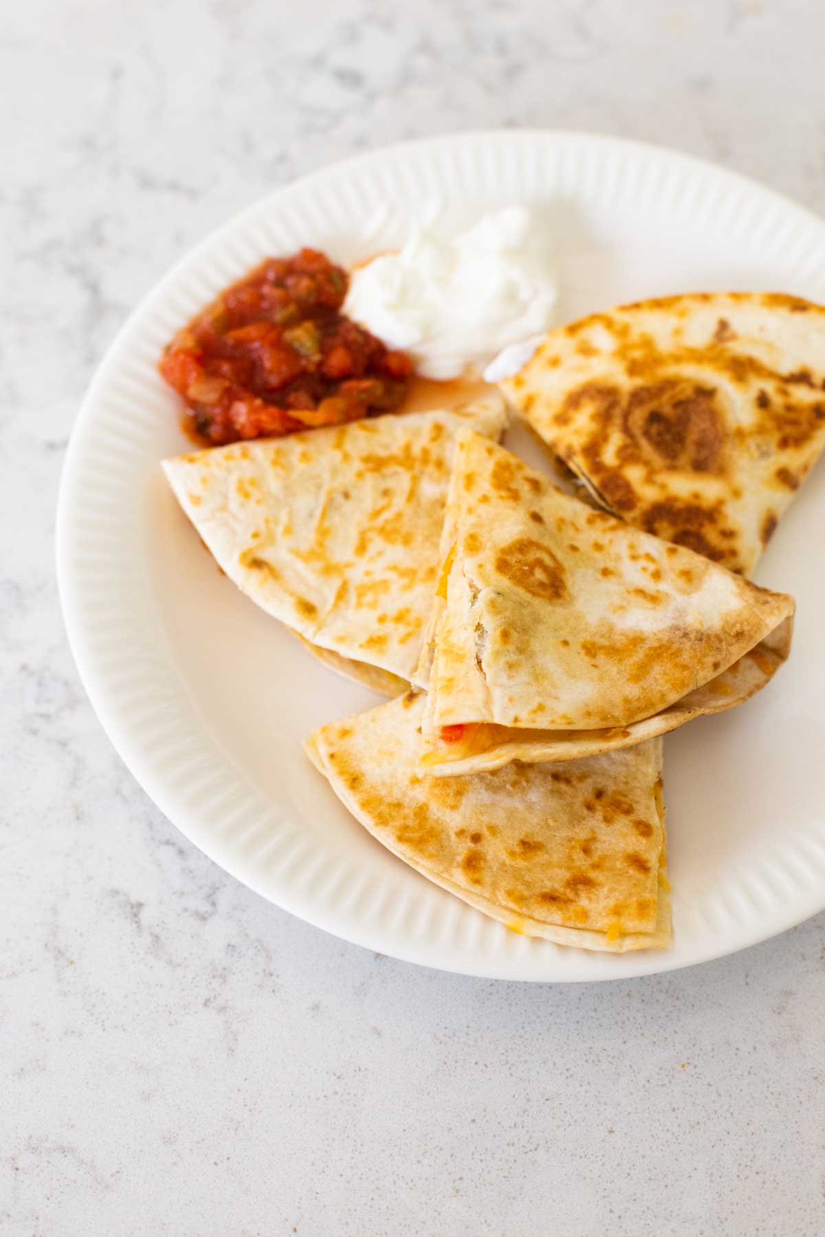 The quesadillas have been served on a dinner plate with a scoop of sour cream and salsa.