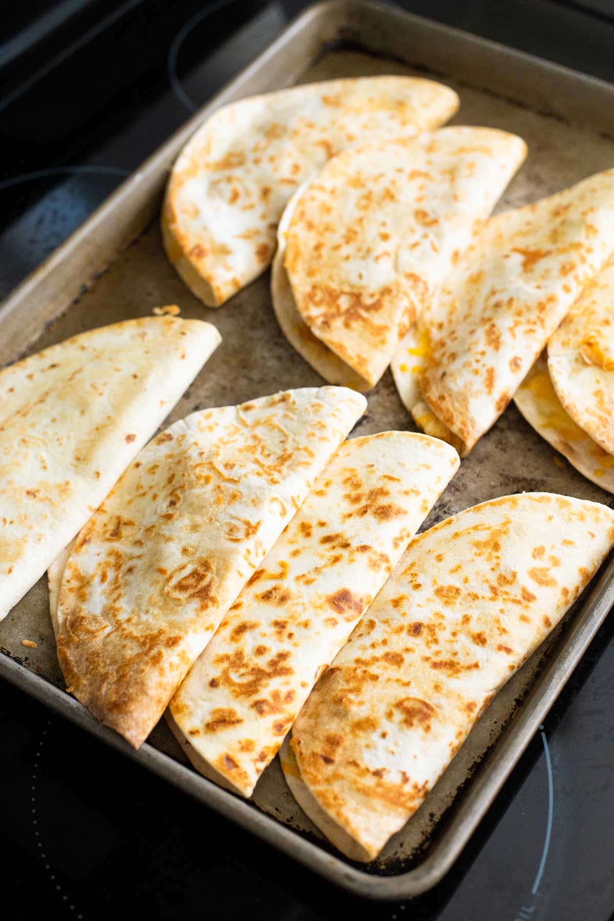 A big batch of quesadillas are on a large baking sheet.