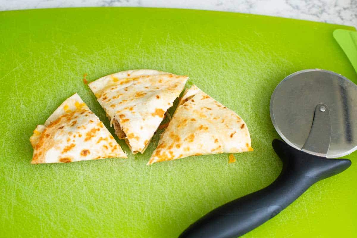 A pizza wheel has cut a quesadilla into 3 triangles.