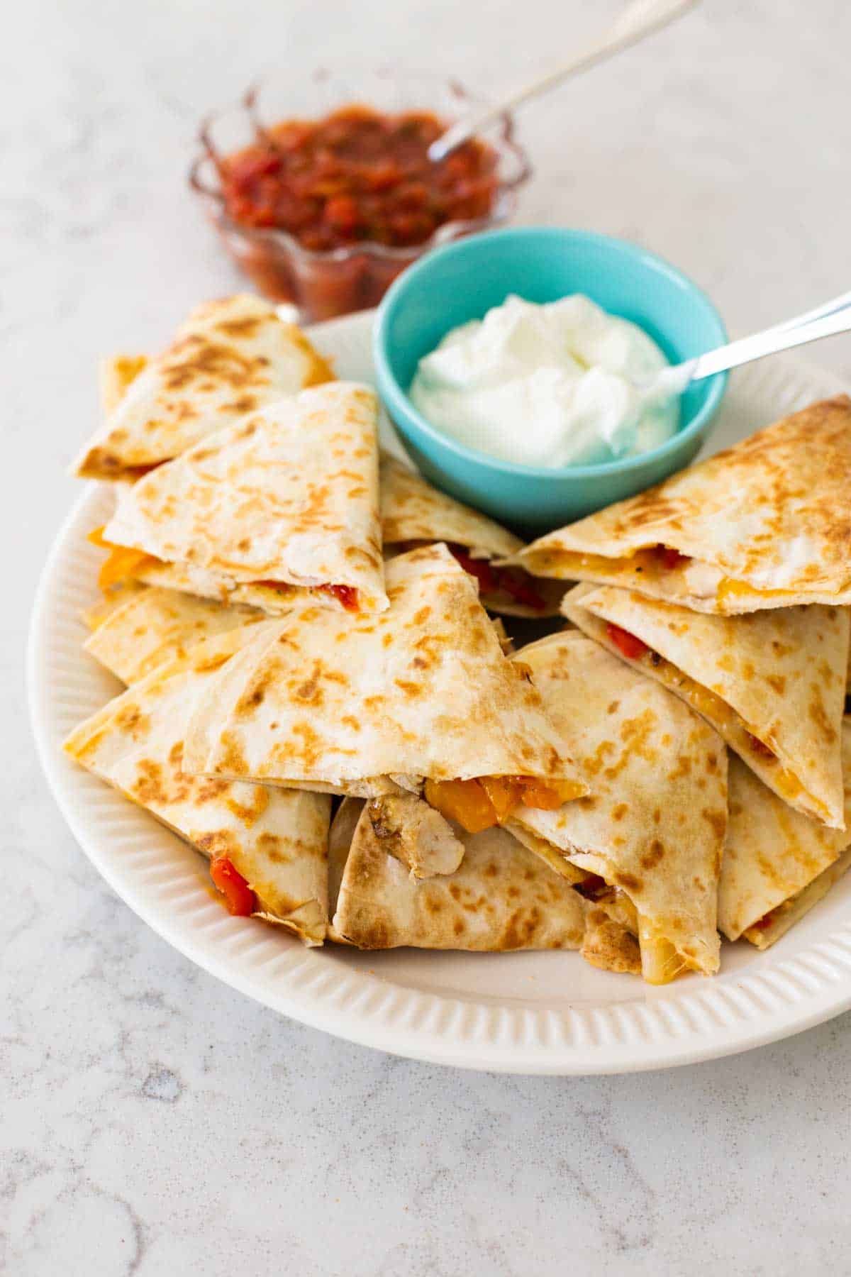 A big family platter filled with quesadillas, a bowl of sour cream, and a bowl of salsa.