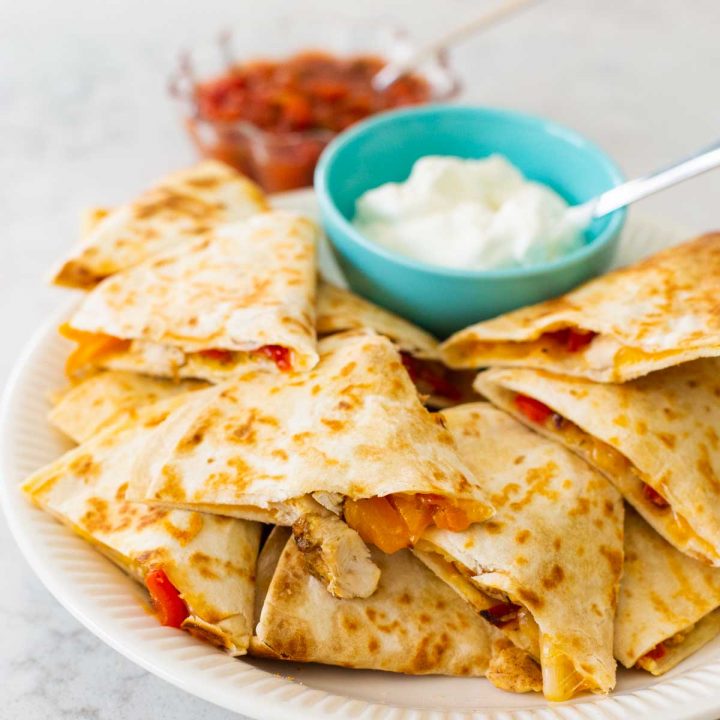 A family platter is filled with jerk chicken quesadillas, a bowl of sour cream, and a bowl of salsa.