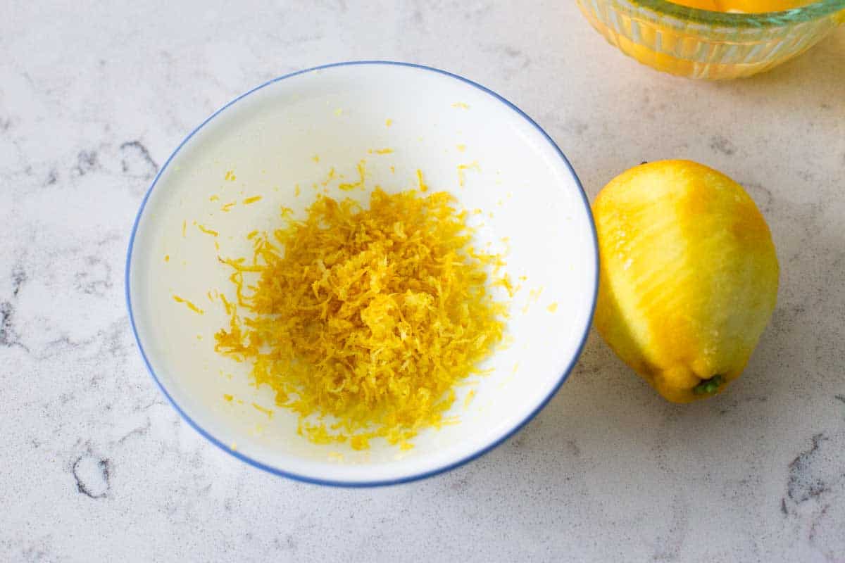 A bowl of lemon zest sits next to a lemon that was used to get the zest.