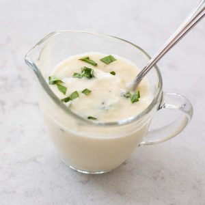 A small pitcher of parmesan cream sauce has fresh basil sprinkled over the top and a spoon.