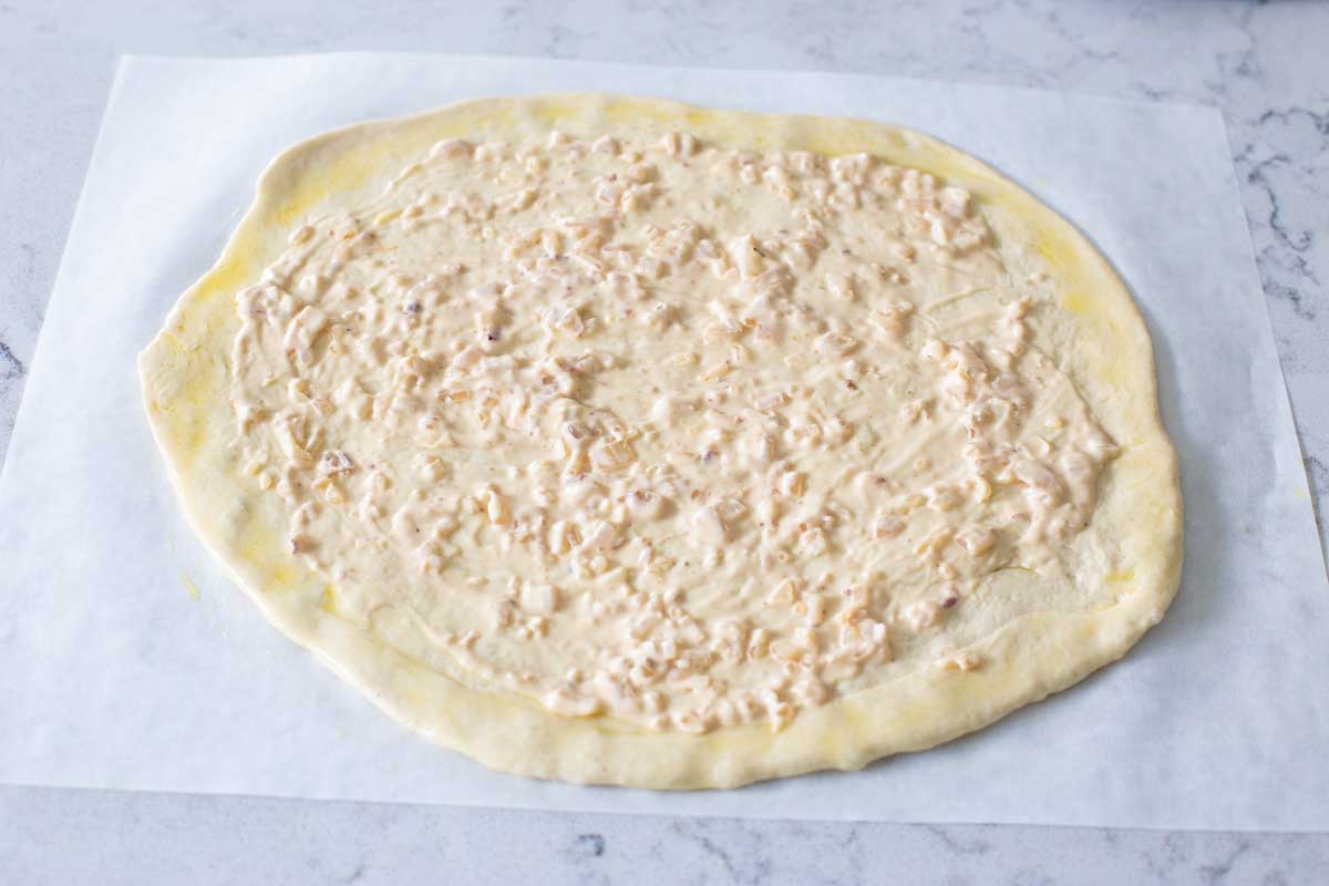 A pizza crust has the white sauce spread over the top.