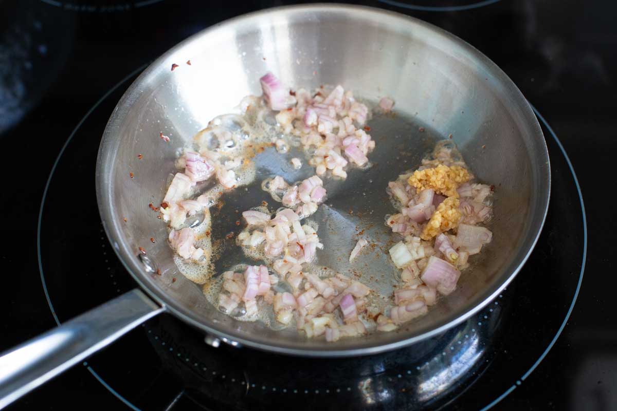 The shallot and garlic are being cooked in the pancetta drippings in the skillet.