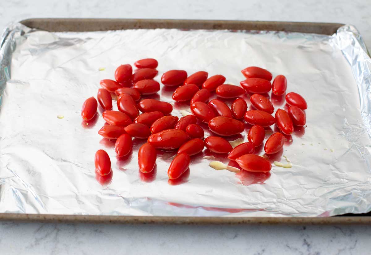 The cherry tomatoes have been tossed in olive oil on a baking sheet.