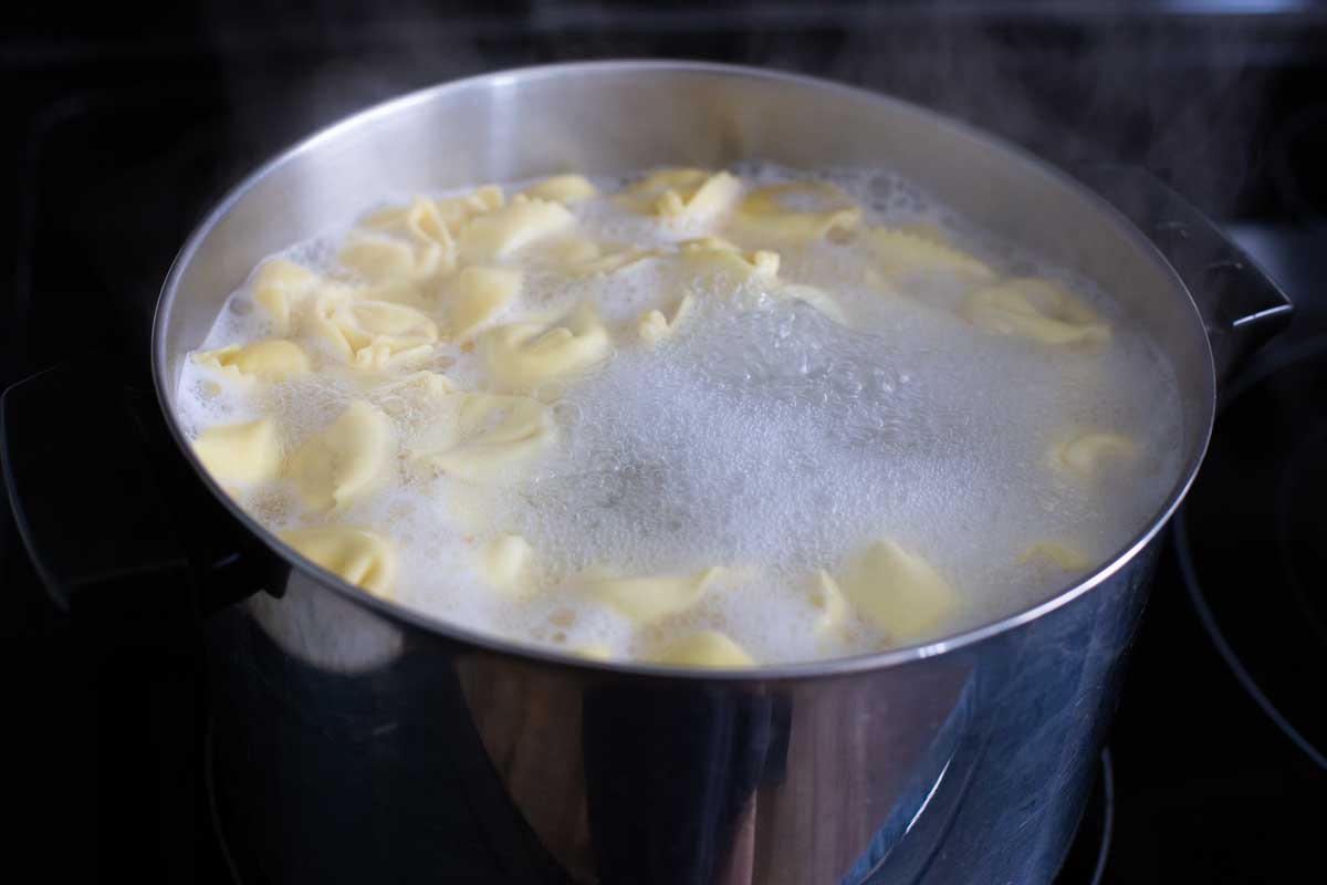 Cheese tortellini are floating in a large pot of vigorous boiling water.