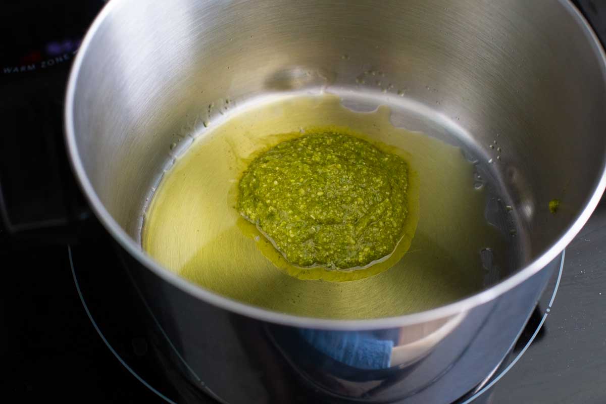 Olive oil is in the pan and a large spoonful of pesto sauce is about to be stirred in.