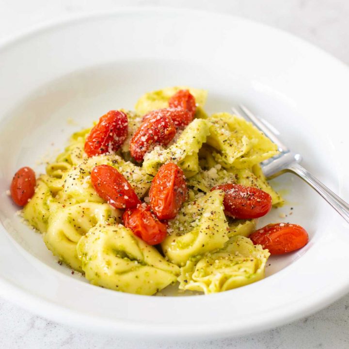 A bowl of cheese tortellini with pesto sauce and roasted tomatoes.