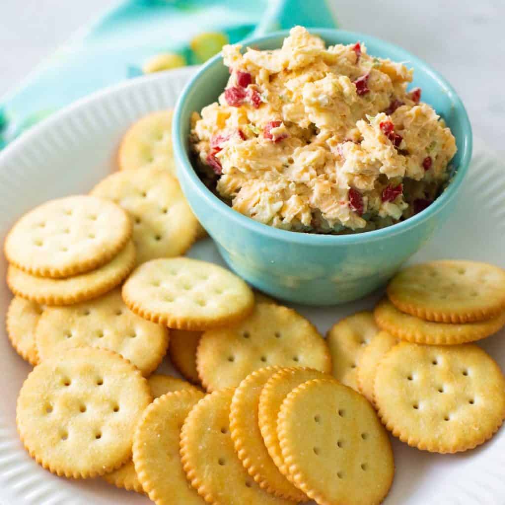 A bowl of homemade pimento cheese is served on a plate with butter crackers.