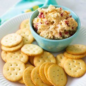 A bowl of homemade pimento cheese is served on a plate with butter crackers.