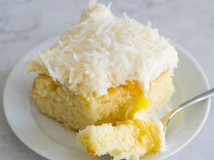 A slice of coconut cake with cream cheese frosting and shredded coconut has a layer of bright yellow pineapple filling.