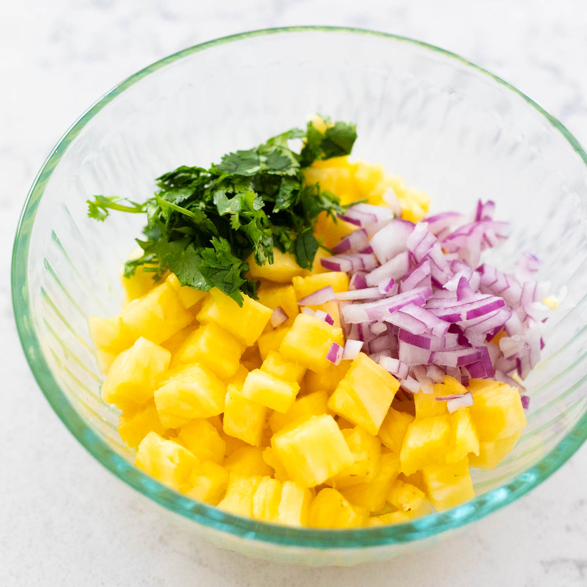 The pineapple, onion, cilantro, and lime juice are about to be stirred together in a mixing bowl.
